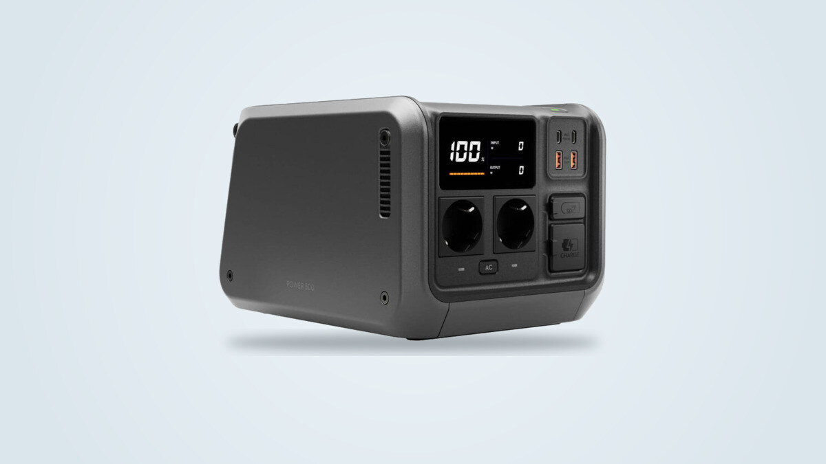 DJI Power 500 portable power station at three-quarter angle, screen lit showing 100%, two AC outlets and SDC port visible