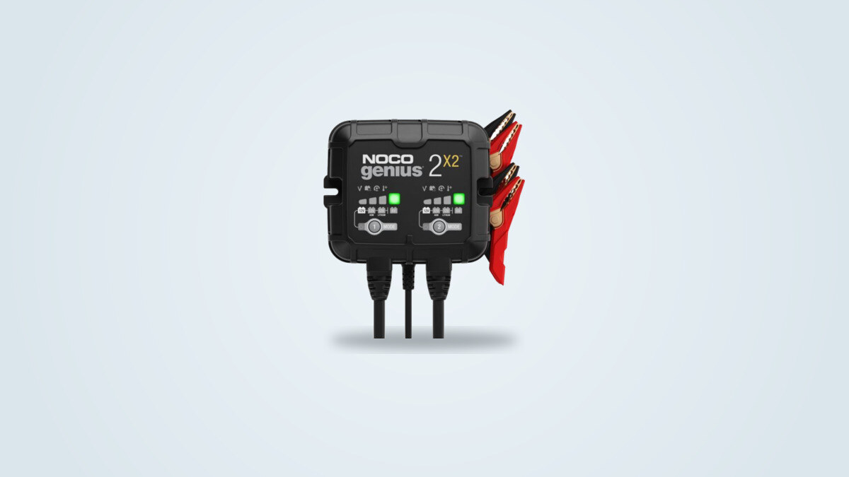 Cargador de batería de doble banco Noco Genius2X2 con sus dos botones Mode y pinzas rojas sobre fondo claro