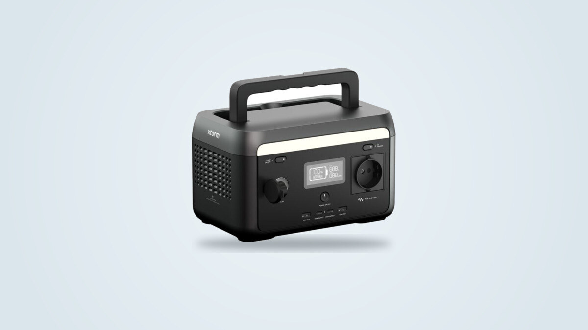 Xtorm XP2W300 portable power station at a three-quarter angle, screen lit showing 100 percent, mains socket and built-in handle visible